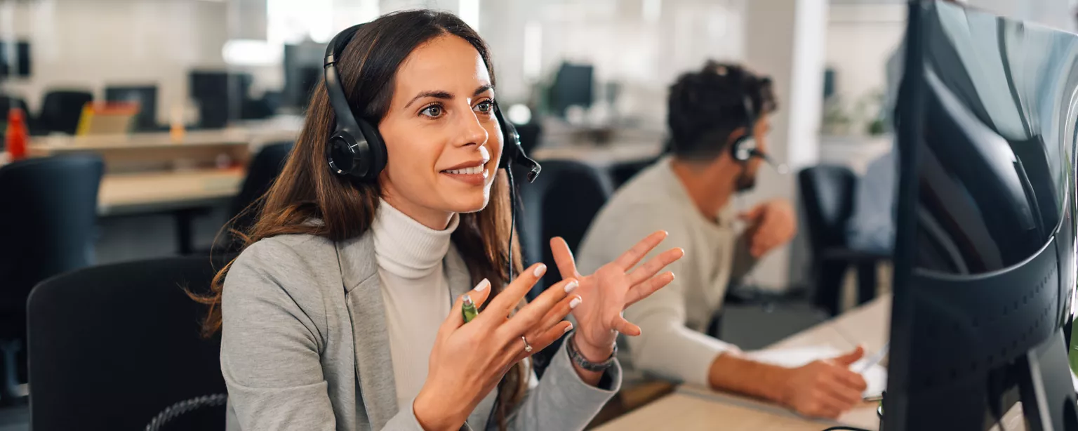 Une femme devant un ordinateur, un casque sur les oreilles, parlant dans le micro du casque tout en tapant au clavier