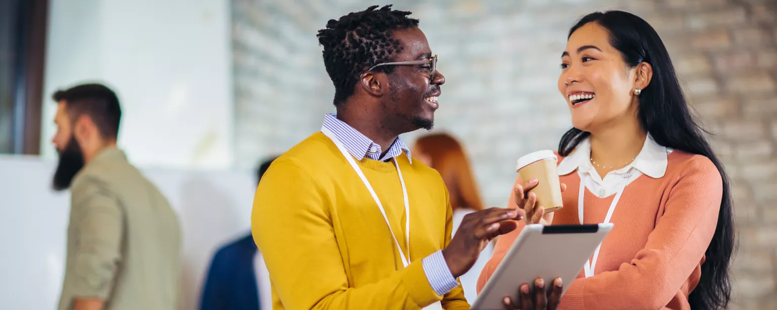 Deux collègues se sourient en discutant du guide salarial Robert Half sur une tablette au travail.