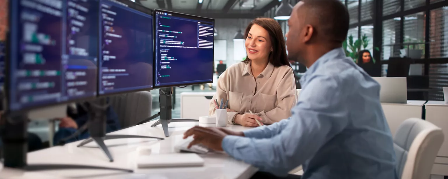 two IT and technology workers sitting in front of their computers working on a project