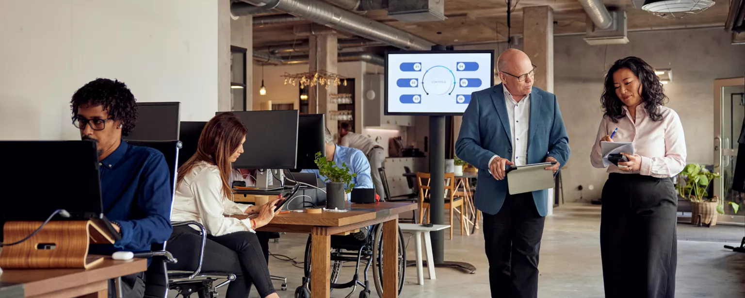 office work place with employees sitting at computer desks and two employees walking together discussing hiring trends