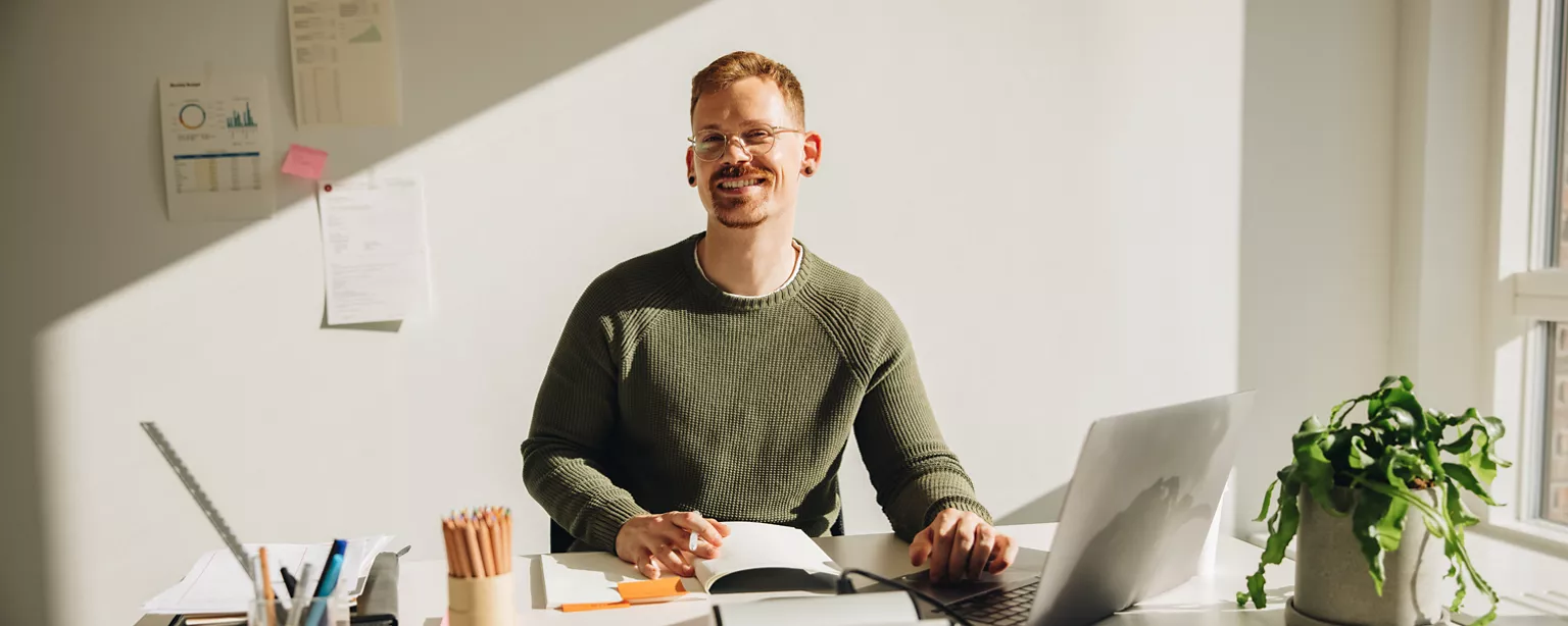 Man sitting at his desk, looking up and smiling at the camera.