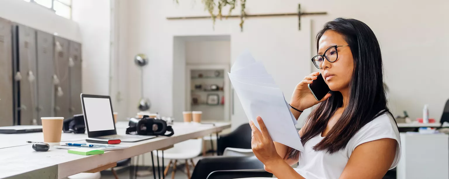 Femme au téléphone à son bureau, regardant un ensemble de documents