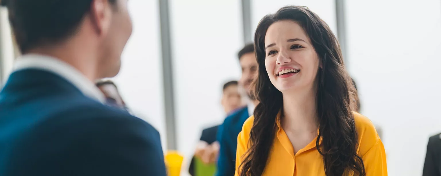 Young woman in yellow top talks animatedly to job interviewer