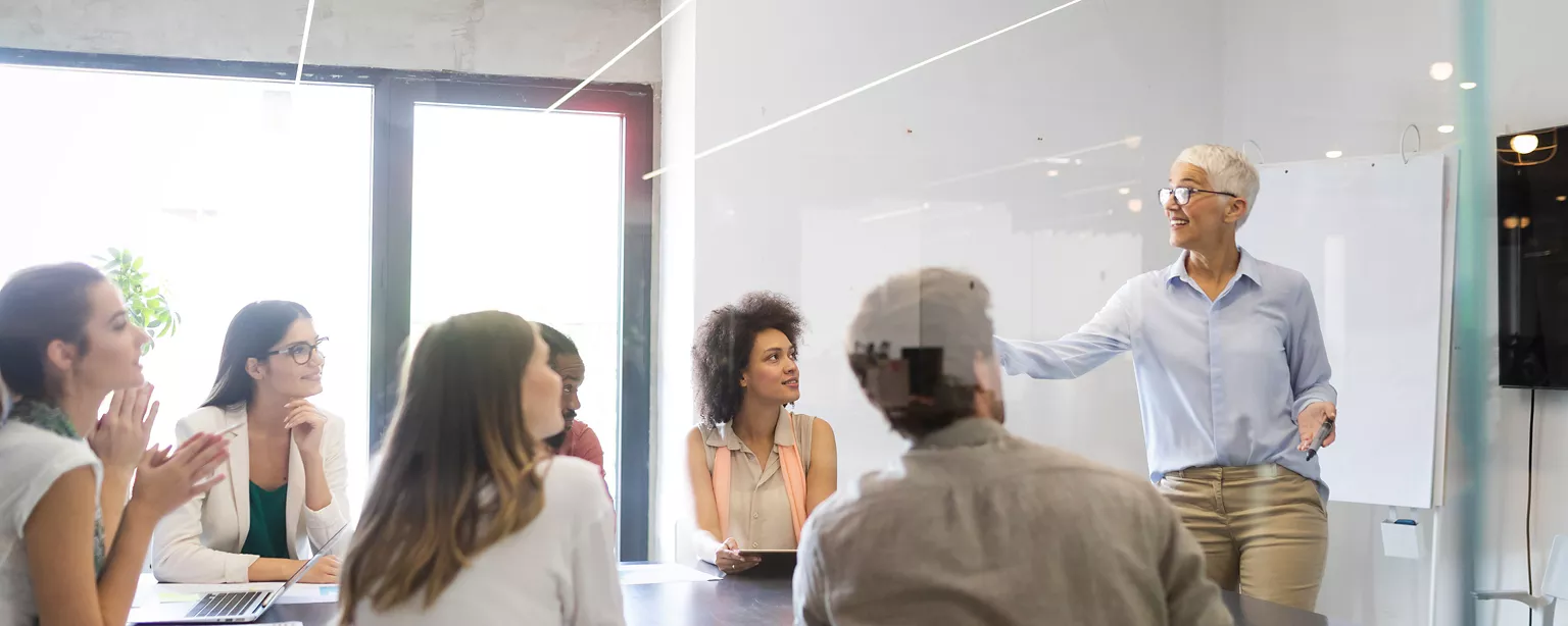 Three people from different generations smile, and the words "examining the multigenerational workforce" appear on a green background overlaying a scene from a workplace.