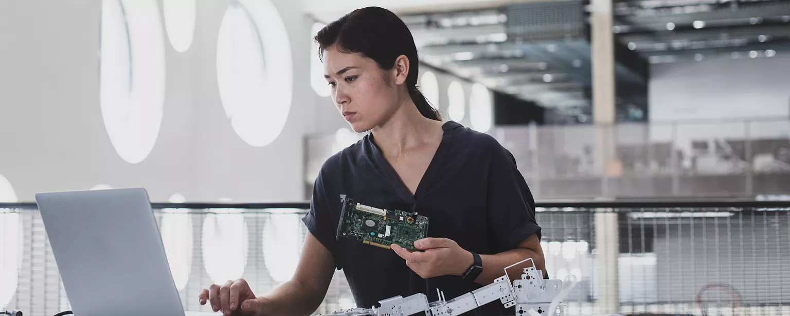 A woman technology professional types on a laptop while working on a robotics project.