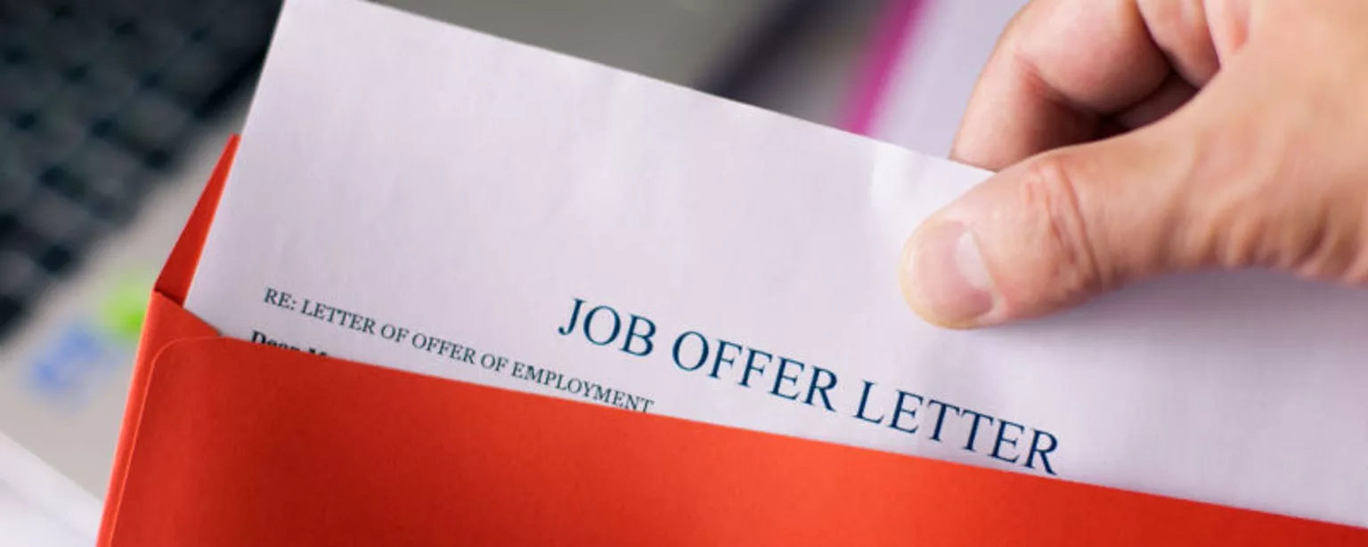 A hand removes a job offer letter from a red envelope.