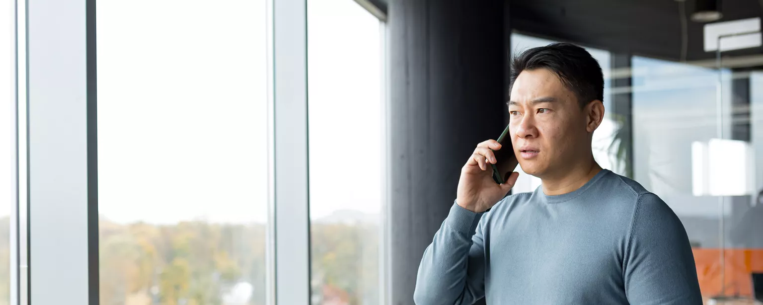 Man standing in front of a window, looking confused, talking on the phone.