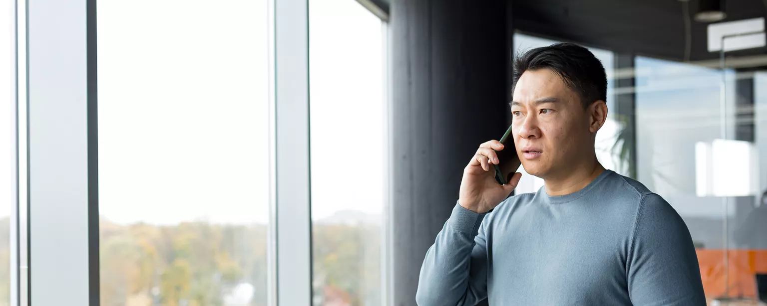 Un homme faisant face à une fenêtre, l'air consterné et parlant au téléphone