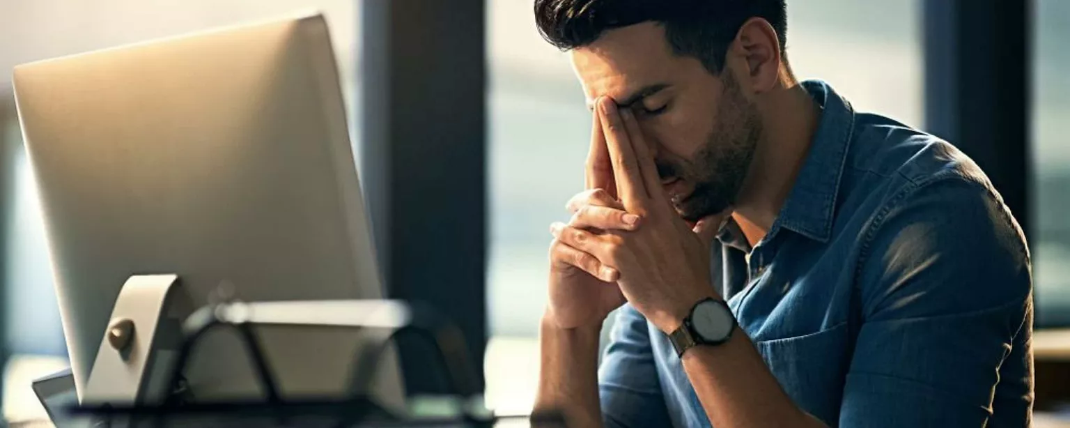 Mann sitzt am Schreibtisch vor Computer und hält müde den Kopf in den Händen