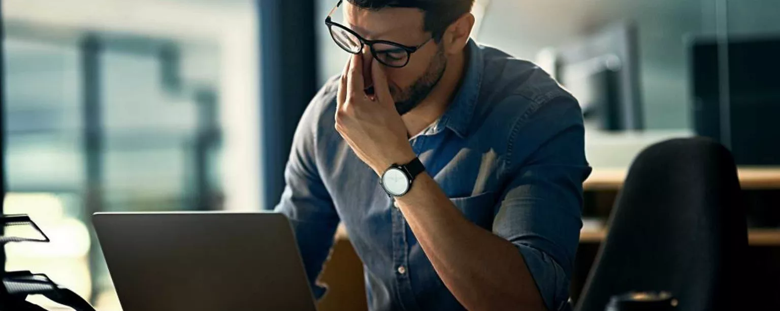 Mann sitzt vor Laptop am Schreibtisch und reibt sich die Augen