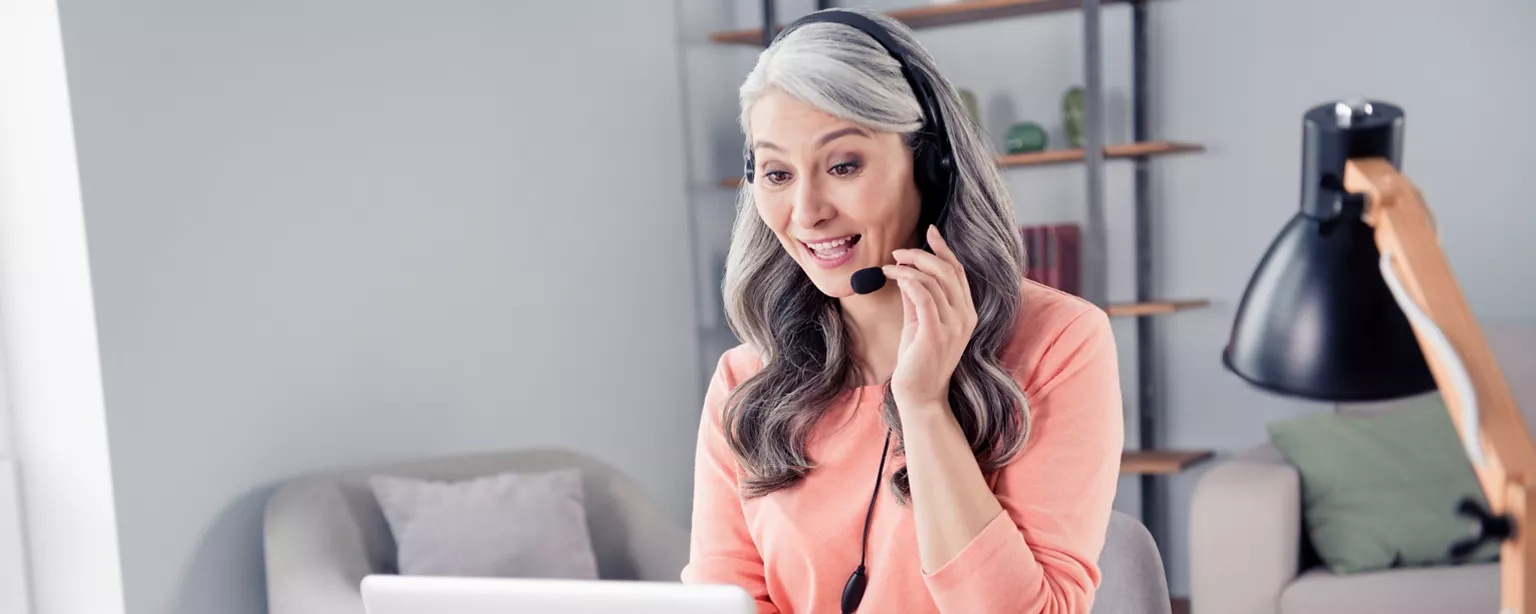A smiling customer service professional wears a headset while working remotely from home.