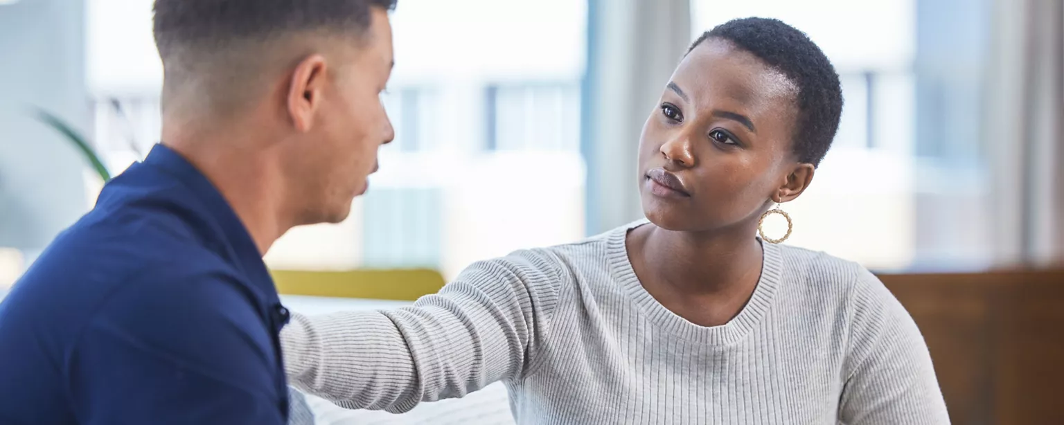 A woman is showing empathy and support by placing her hand on a man's shoulder while listening attentively during a conversation.