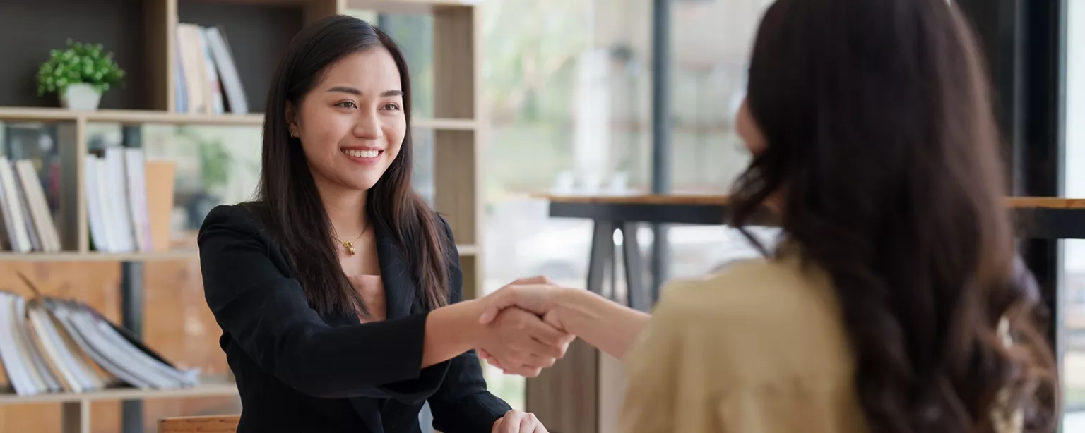 A young professional smiles while shaking hands with a recruiter after a successful salary negotiation.