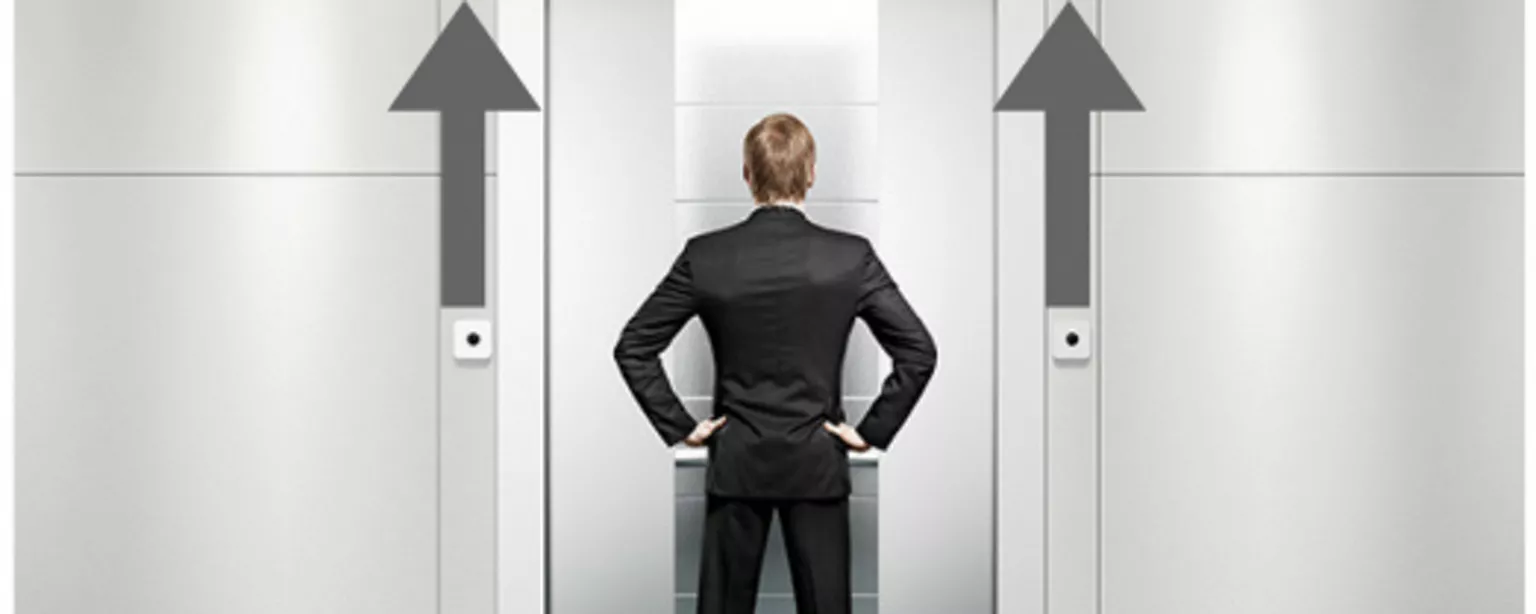 A man stands in front of elevator with 2 arrows pointing up