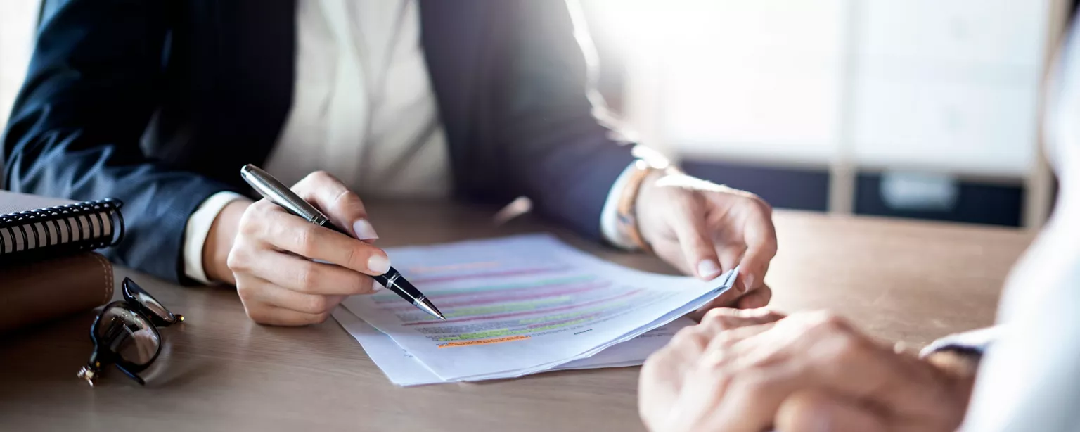 Two professionals review highlighted financial documents in a meeting.