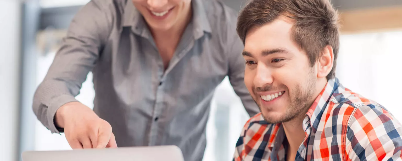 Two young, smiling IT professionals looking at a laptop. 