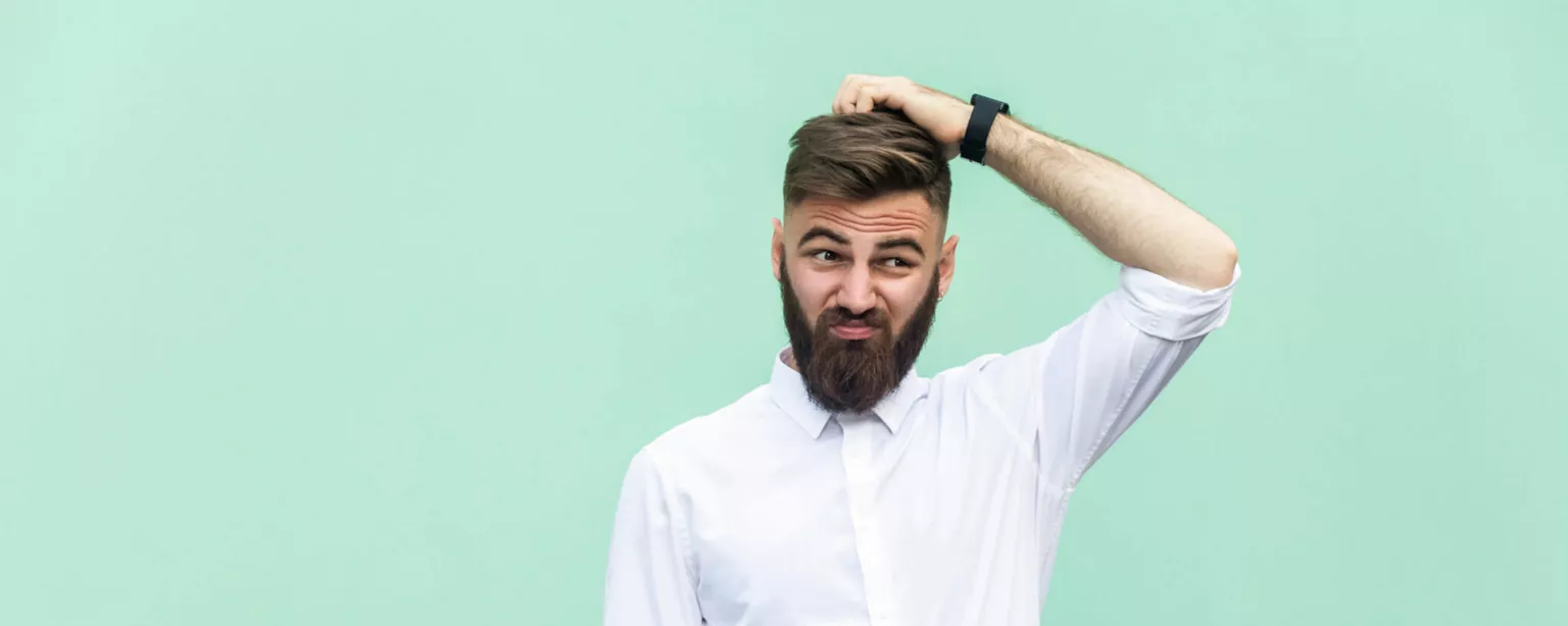 A man with a beard looks perplexed while scratching the top of his head.