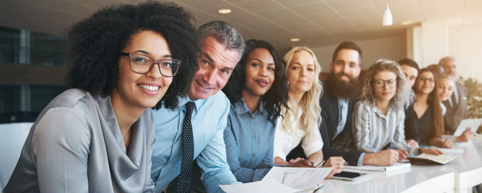 Several employees of diverse backgrounds and ages seated at a long conference table smiling