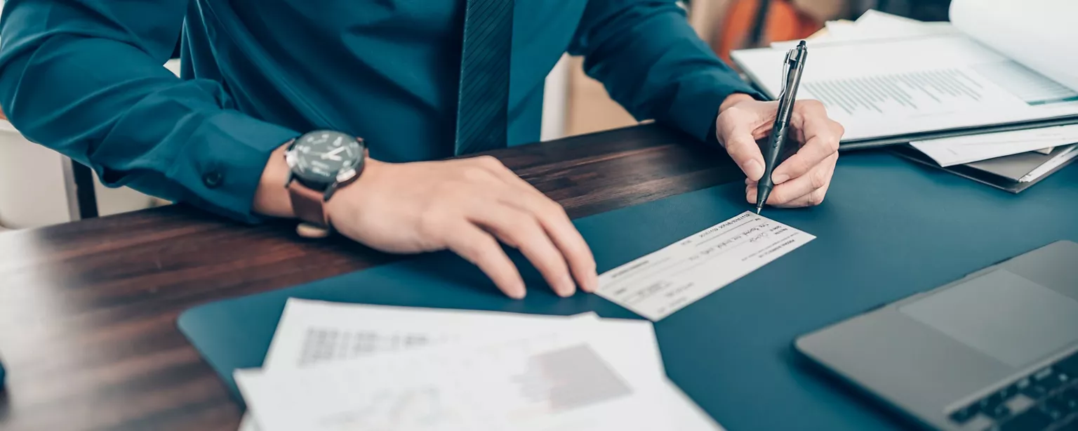 Payroll professional signing a paycheck at a desk with financial paperwork.