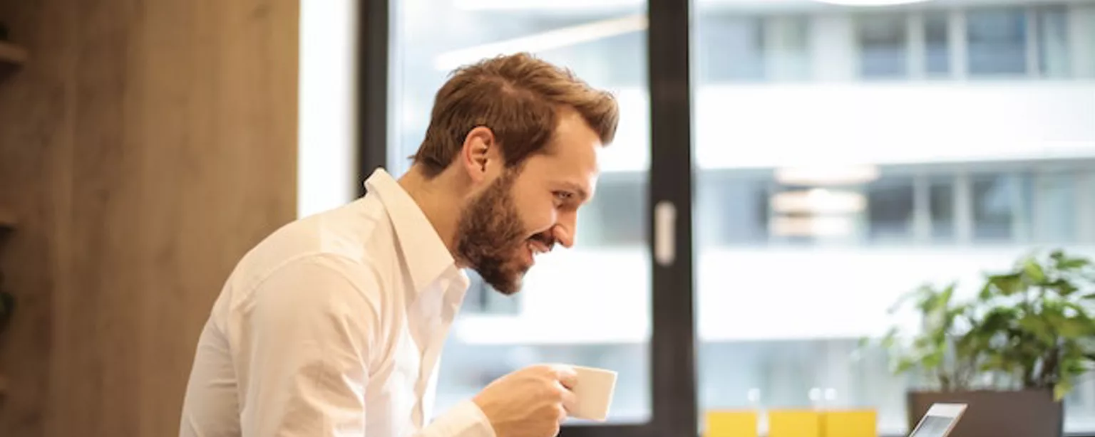 Mann in Businesskleidung sitzt vor Notebook und freut sich 
