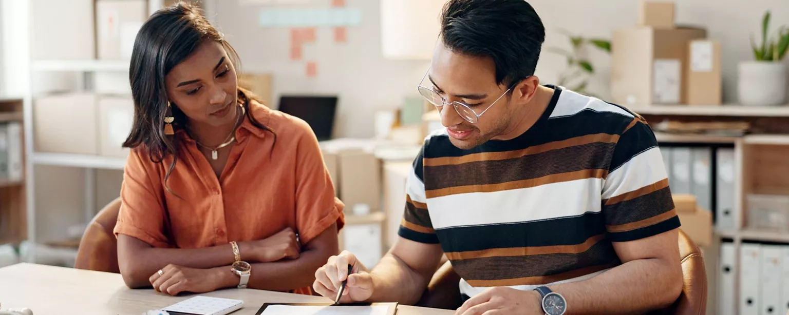 A man and woman collaborate at a desk, reviewing their company’s legal compliance checklist together in an office.