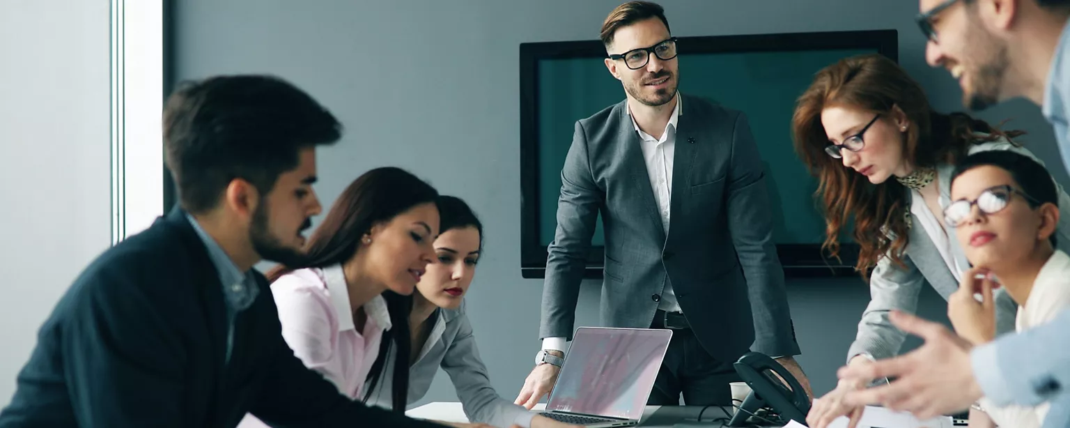 Business professionals around a conference table collaborate during a strategy meeting while a team leader presents ideas.