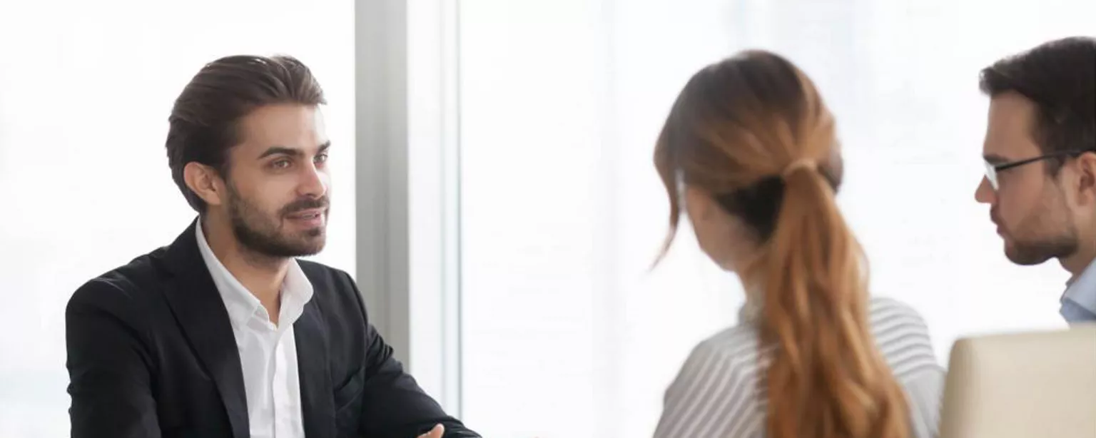 Young man talking to interview panel with hands stretched out.