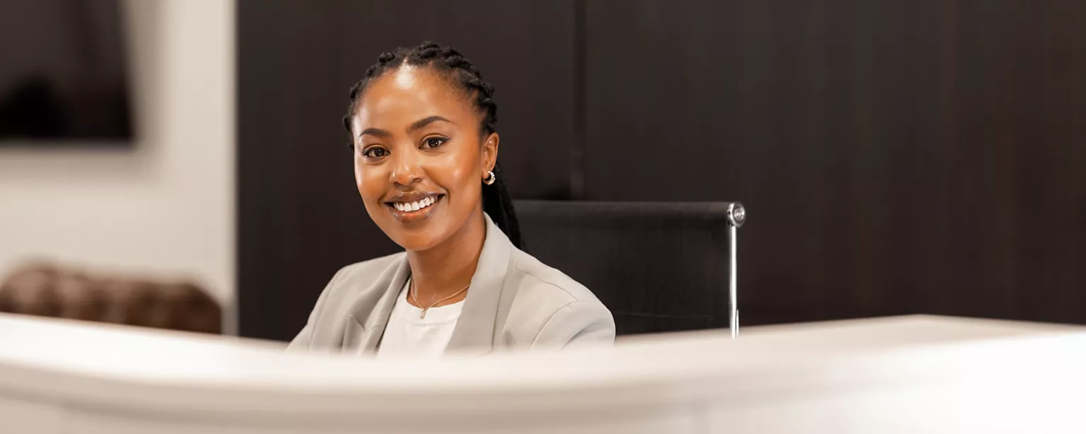 A talented receptionist smiles as she looks over a large monitor in the foreground.