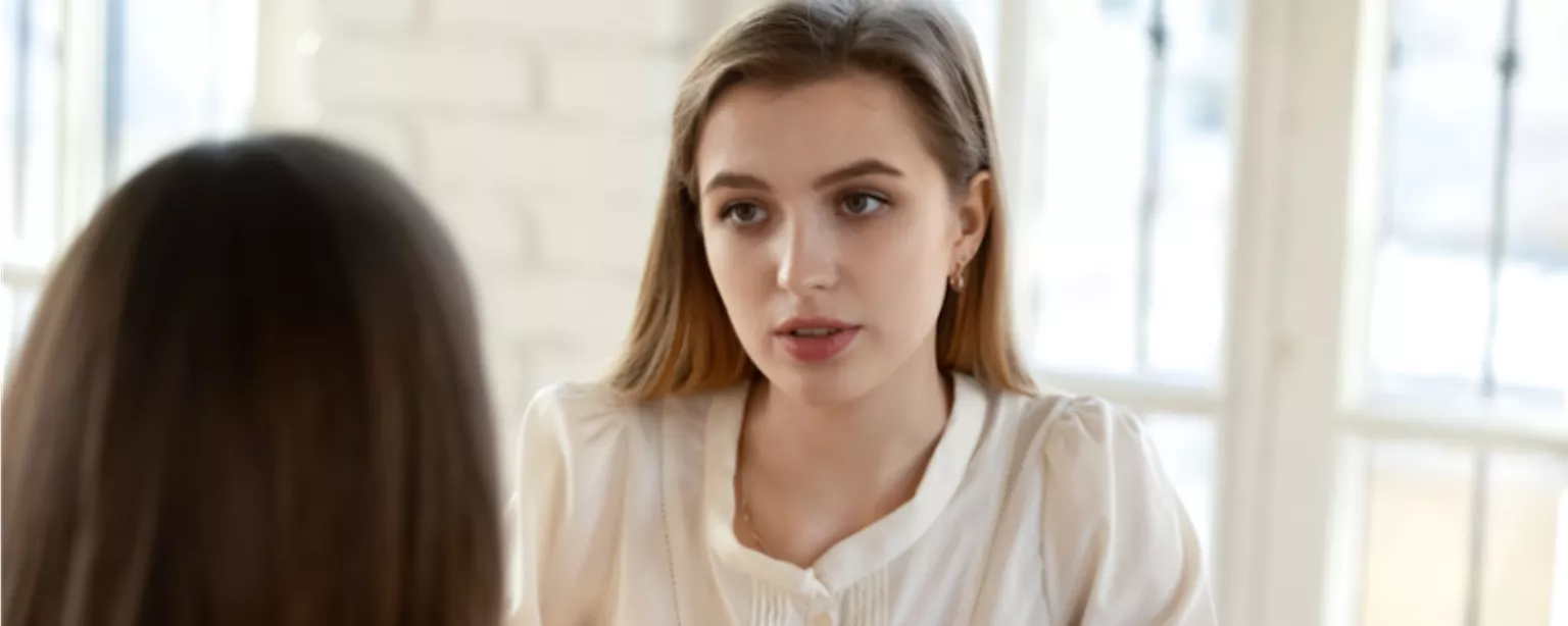 Woman in a beige blouse in a job interview answering a question.