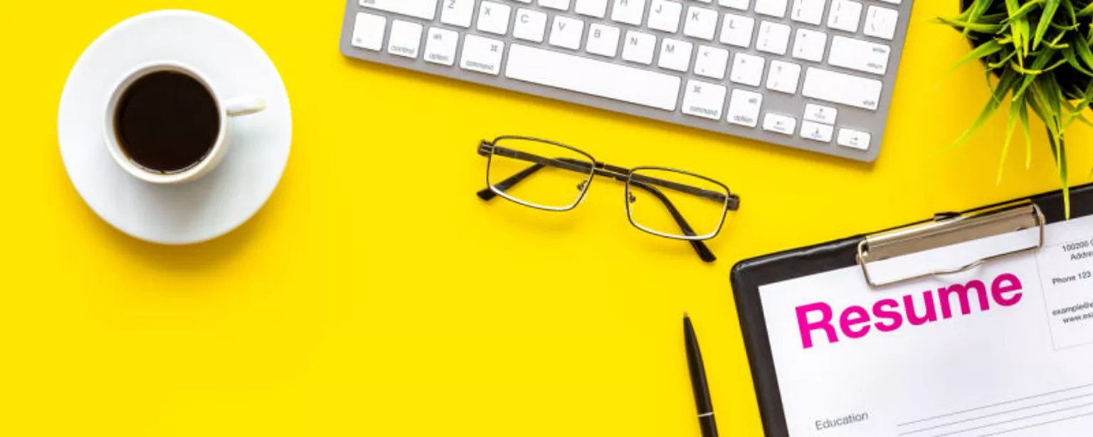 resume sitting on a bright yellow desktop next to keyboard, reading glasses and a cup of coffee