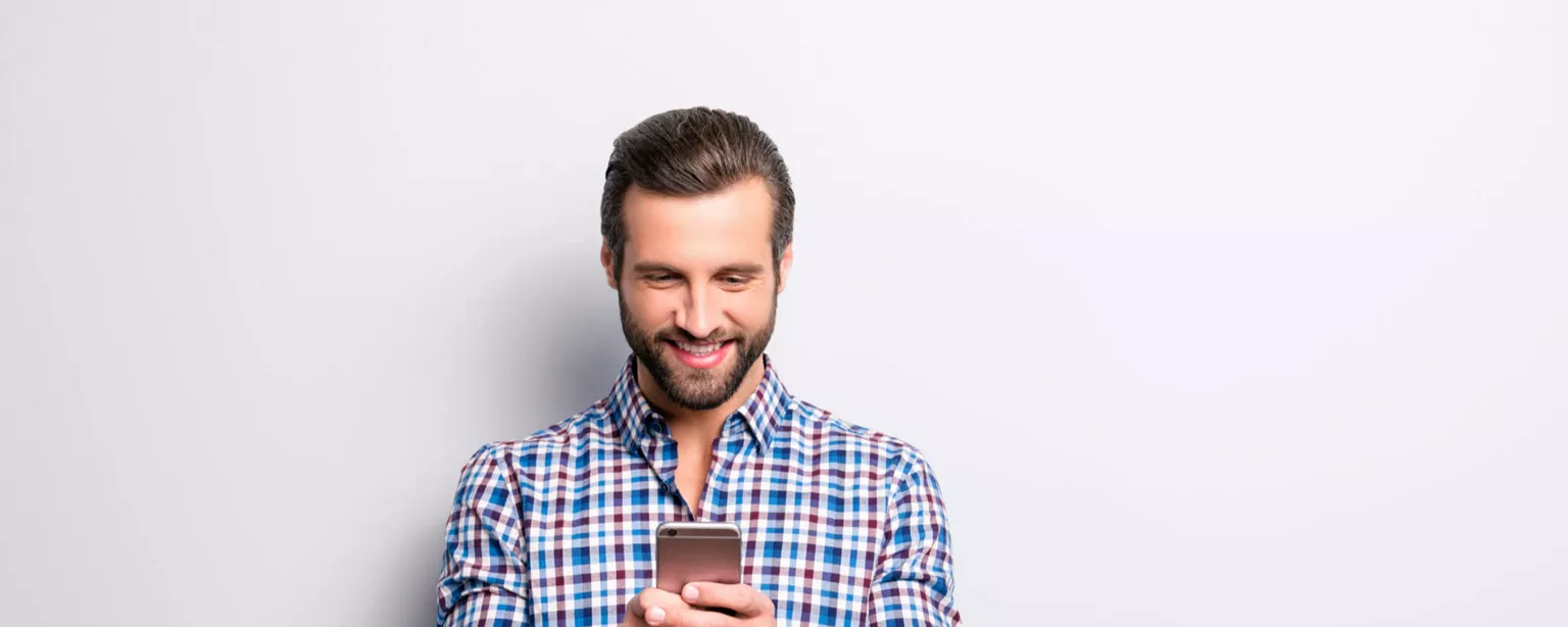 A man looks at his mobile phone, smiling at what he sees.