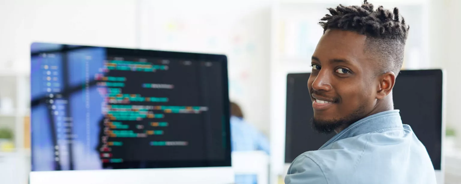 A young man, who is a software developer, working on code and smiling toward the camera.