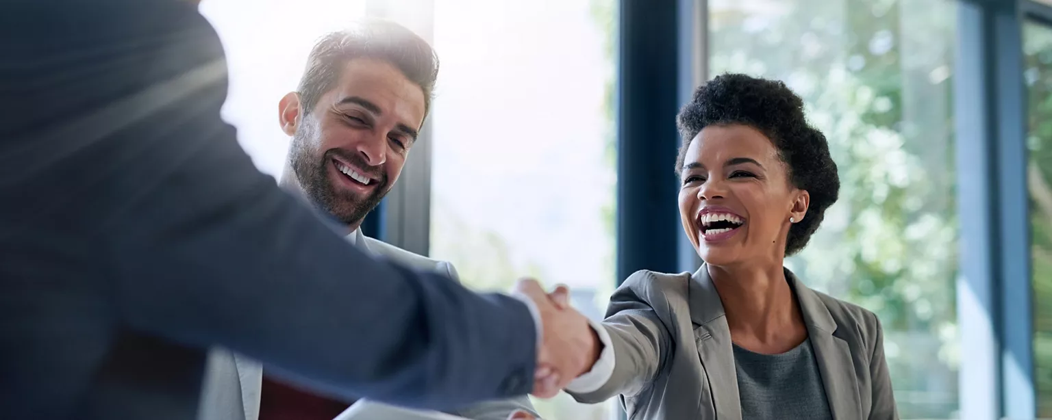 A happy full-time engagement professional shakes hands with an associate as another happy colleague looks on.