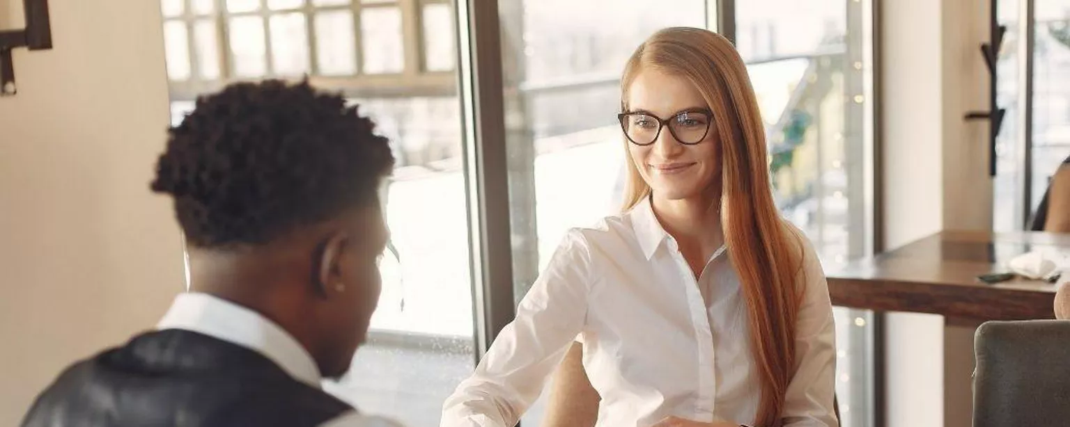 Eine junge Frau sitzt einem Gesprächspartner am Tisch gegenüber