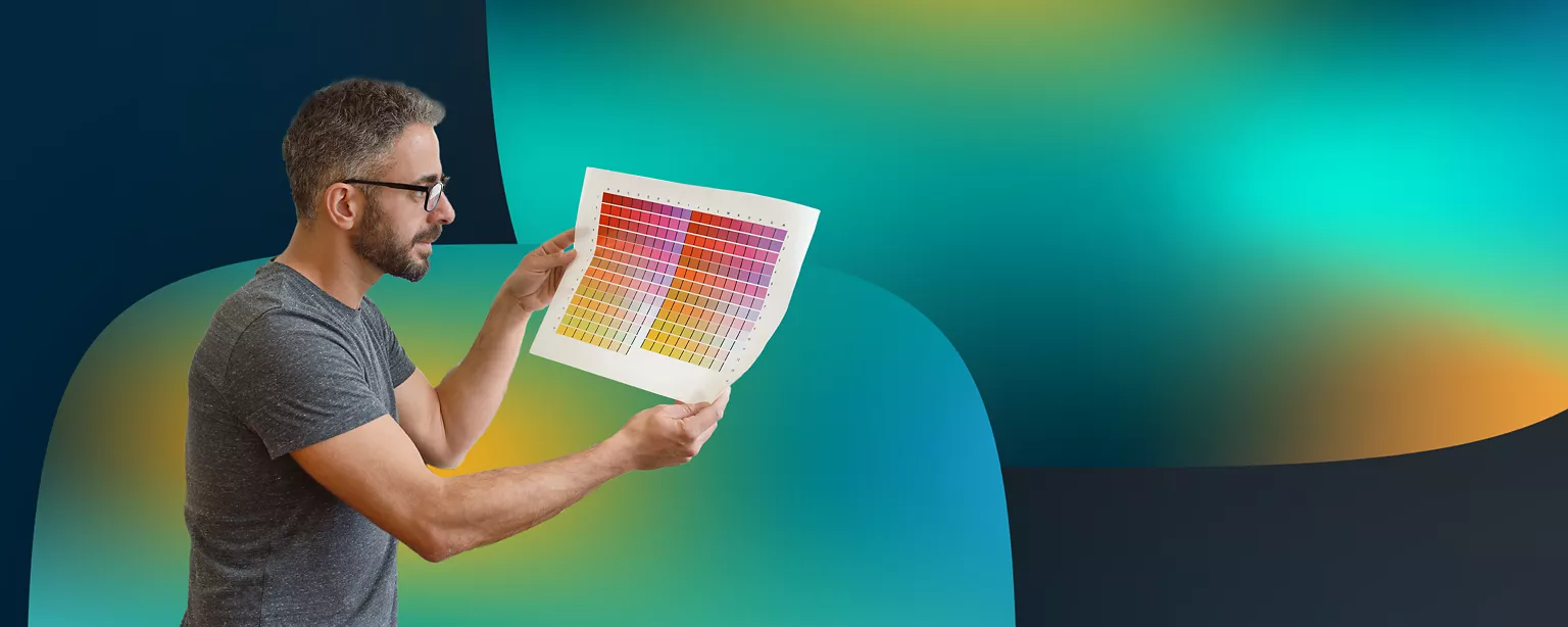 A man wearing glasses and a gray shirt holds a colorful piece of paper and looks intently at it.