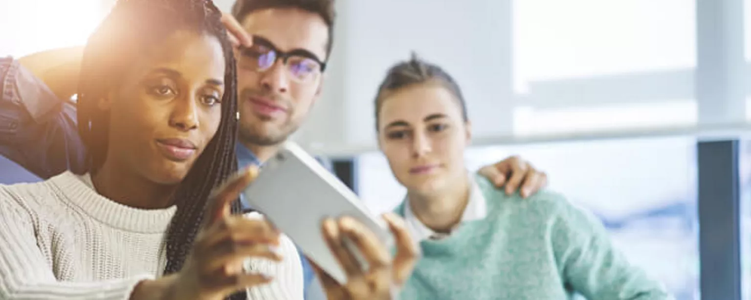 Image of three creative professionals looking at Snapchat on a smartphone.