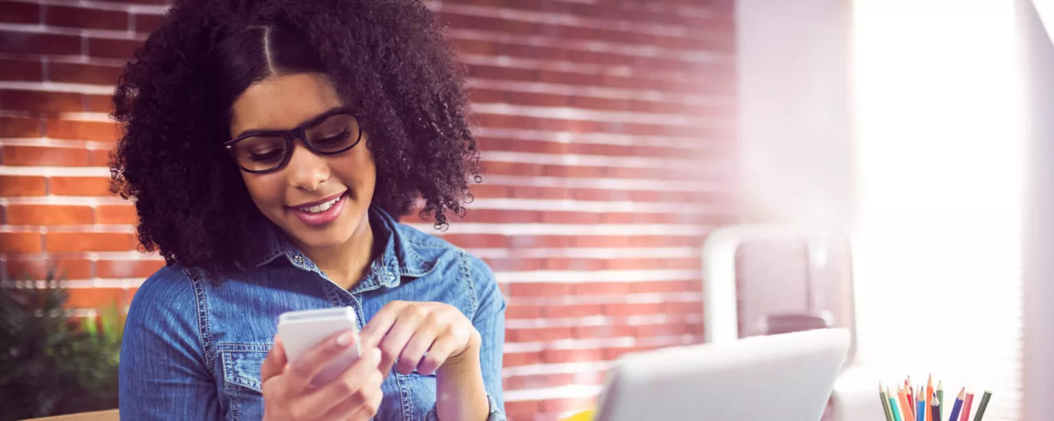 Photo of a woman at her desk using social media for recruiting on her smartphone.