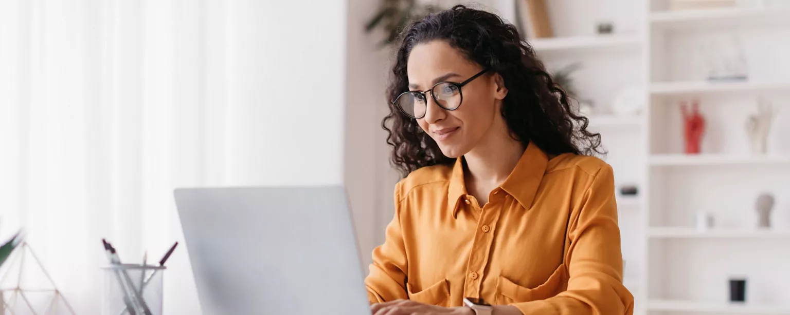A woman smiles as she works on her resume on a laptop.