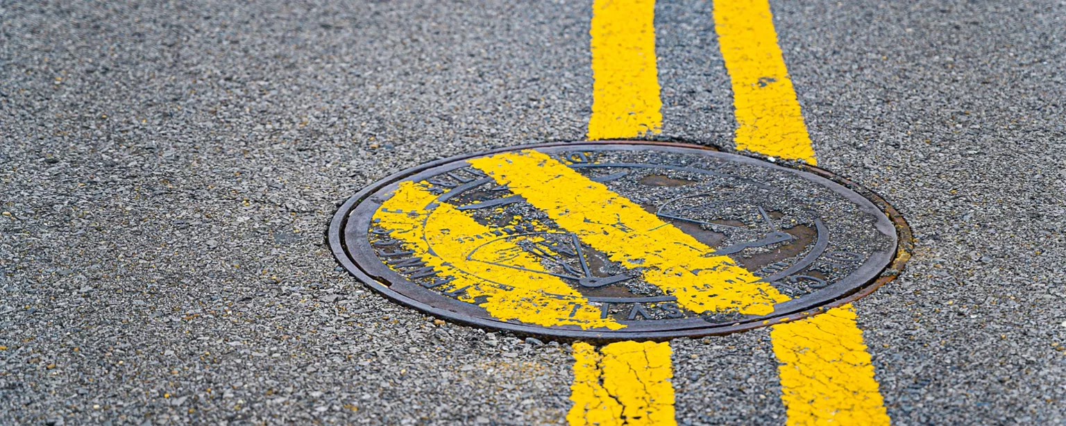 An image of yellow stripes painted over a maintenance hole lid, with the lid turned askance., after someone made a mistake at work.