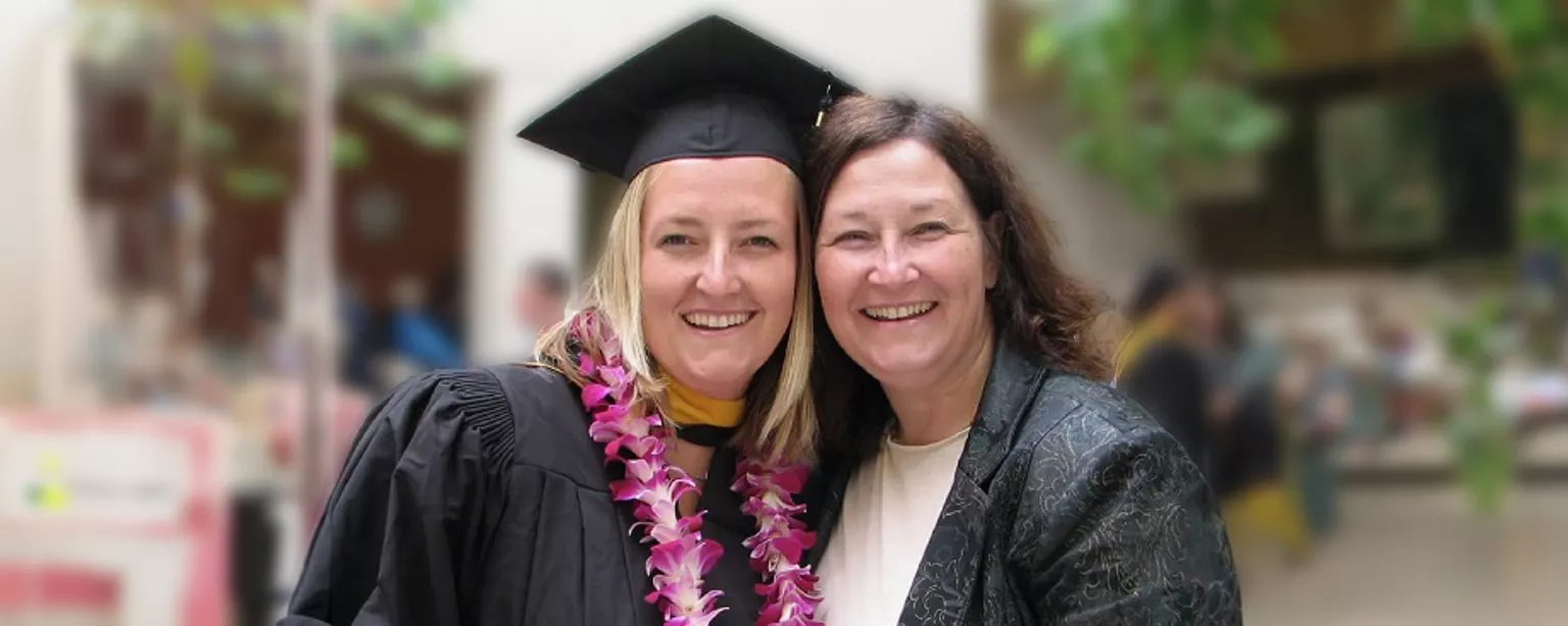 Stephanie Dolmat in black cap and gown standing next to her mother at her Master's Degree graduation ceremony.