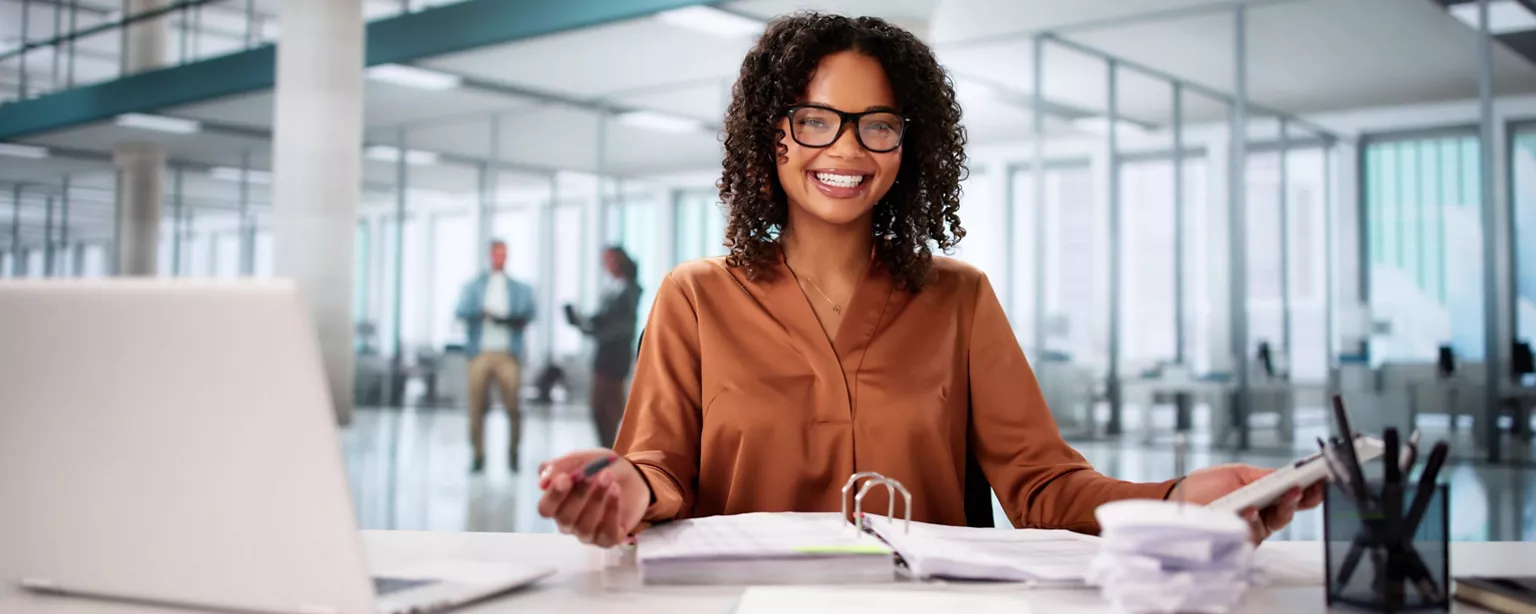 A tax accountant wearing glasses reviewing financial documents with a laptop and calculator on the desk.
