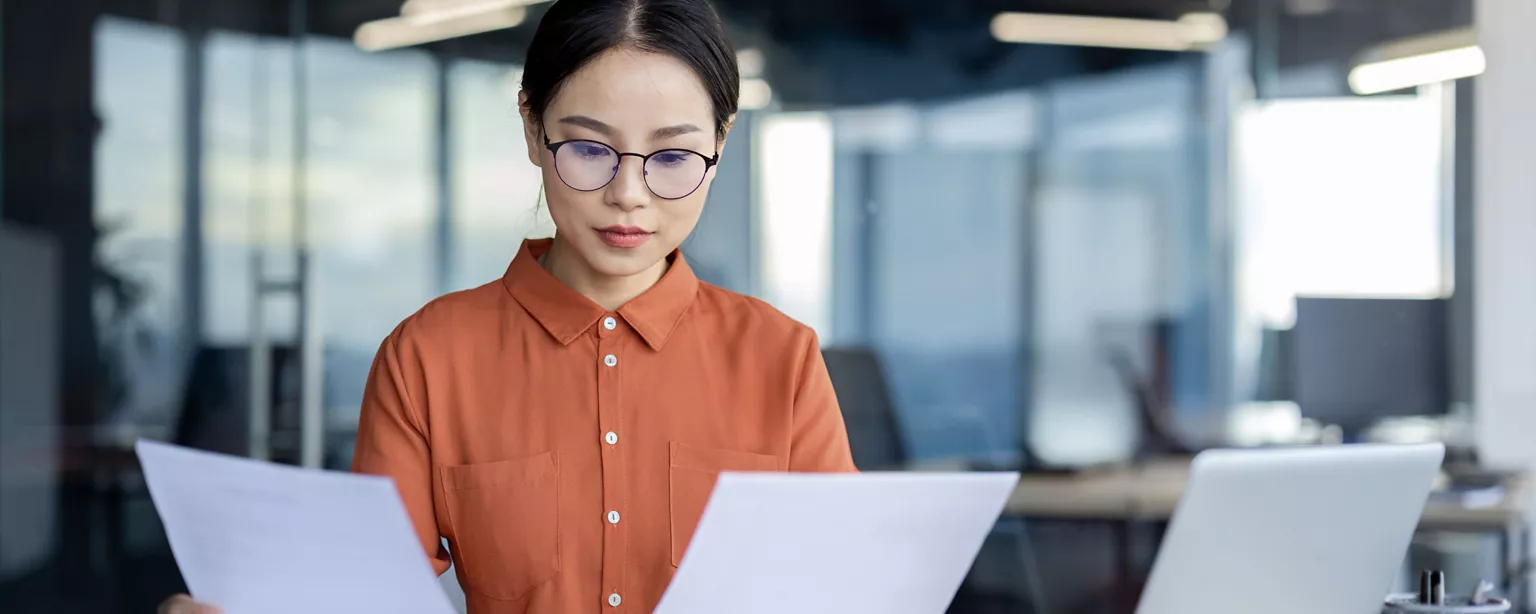 A focused professional in an orange blouse reviews documents in an office.