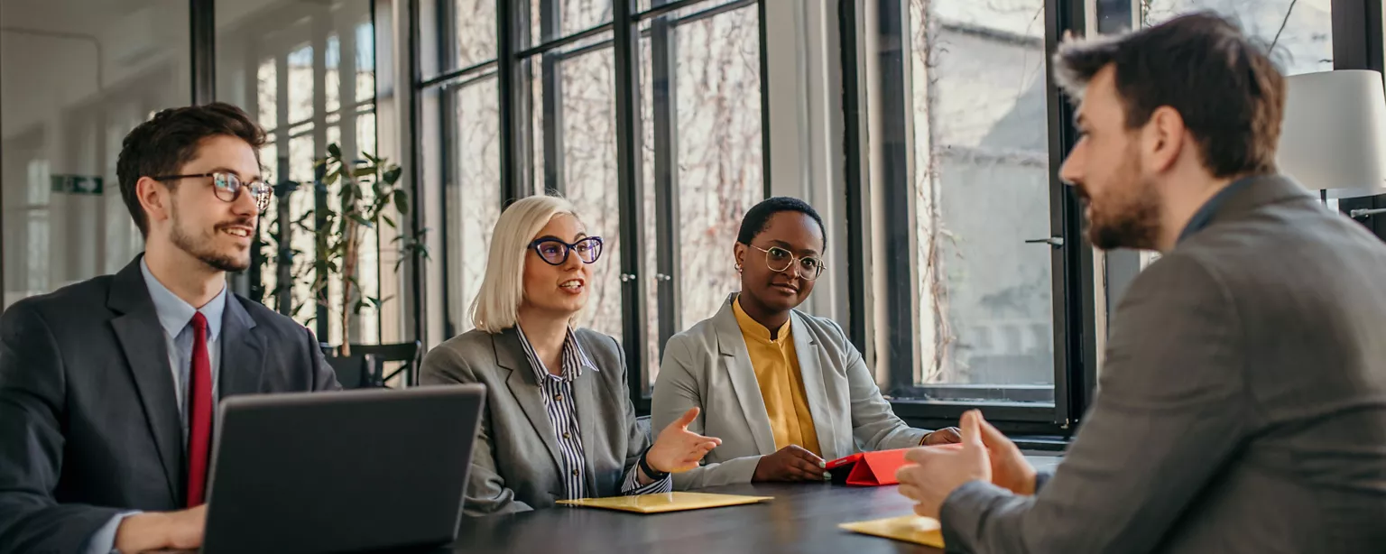 Three HR professionals in a business meeting discuss something with a candidate across the table in an office conference room.