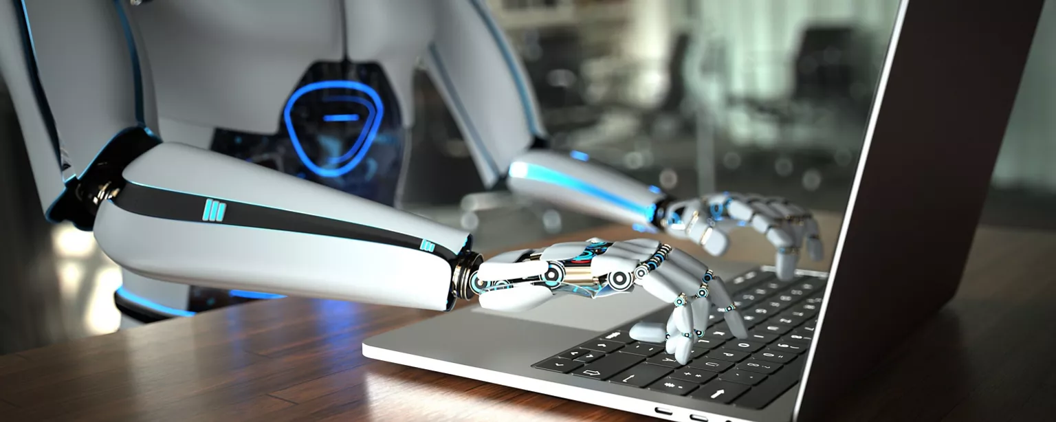 A humanoid robot types on a laptop keyboard in an office.
