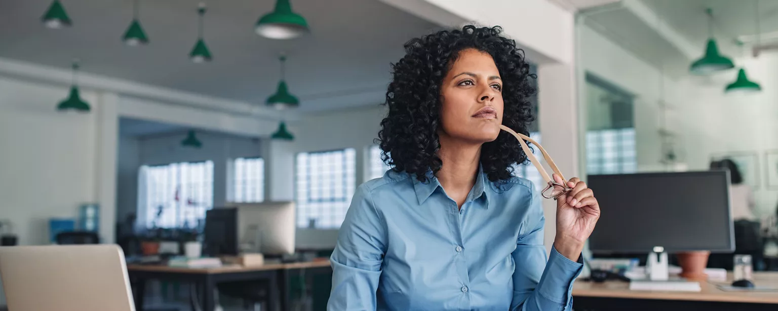 A woman in an office holds her eyeglasses as she thinks over the risks and benefits of accepting a counteroffer. 