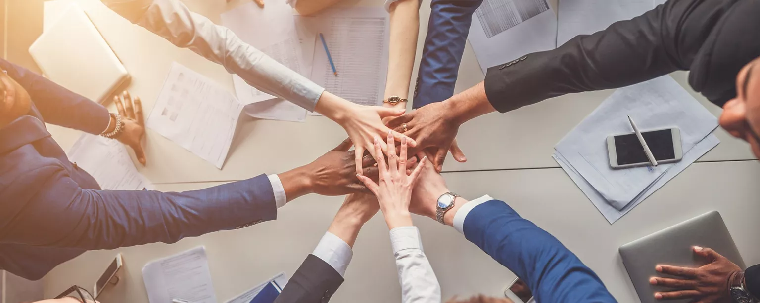 Team members at a small business placing their hands together in a show of collaboration around a table.