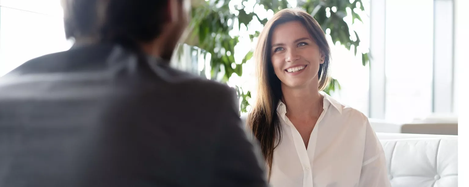 A smiling job candidate sits facing a hiring manager as they talk during an interview.