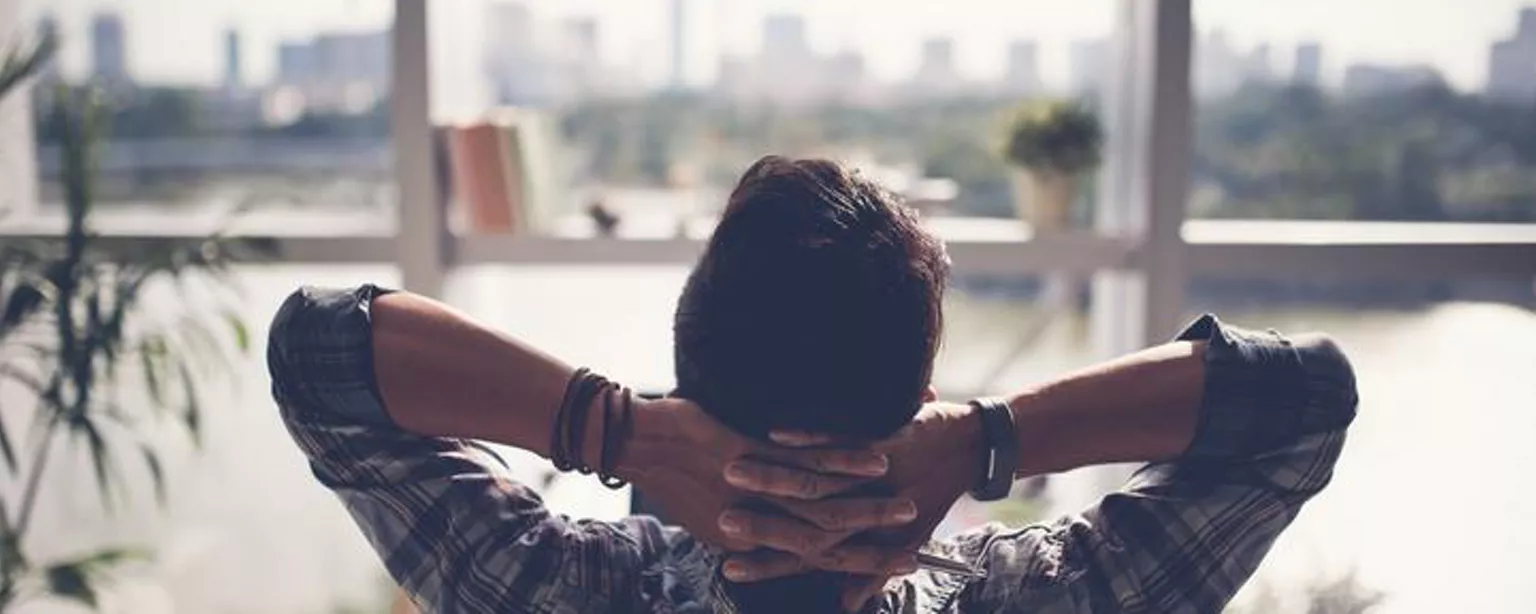 A man looks relaxed out the window with his arms behind his head