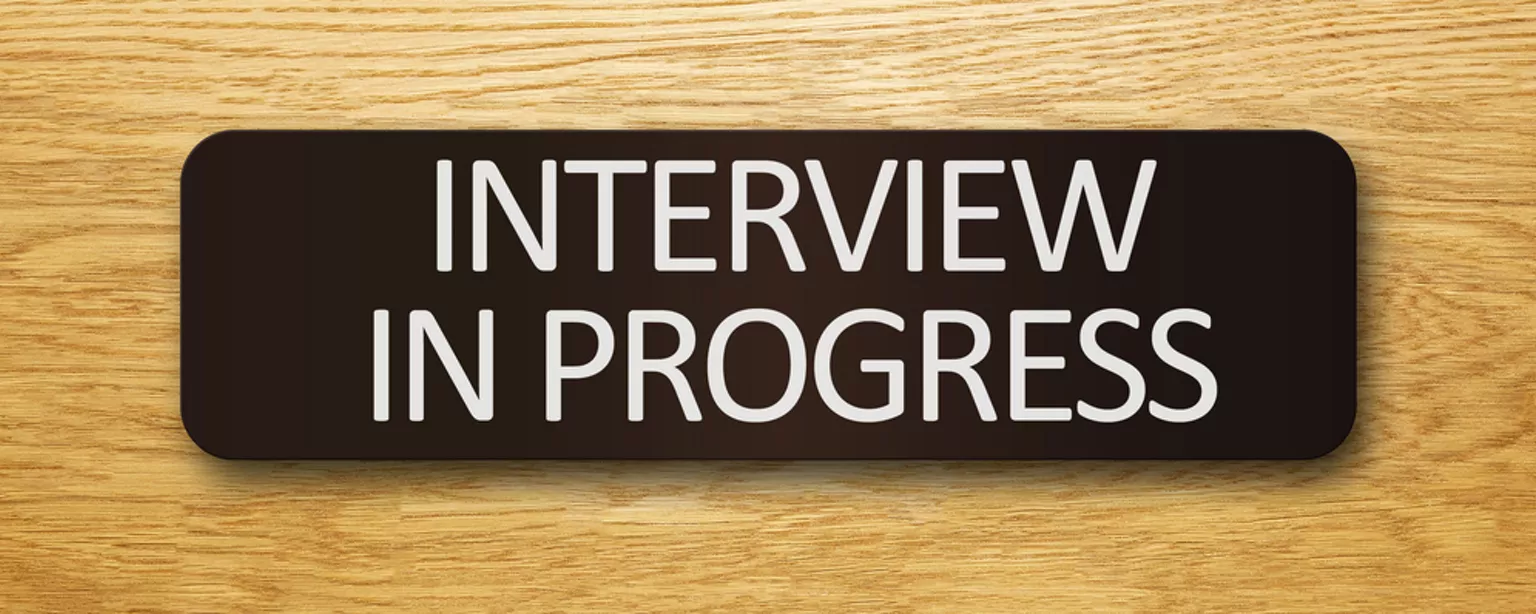 A sign reading "Interview in Progress" is visible on a wooden background.