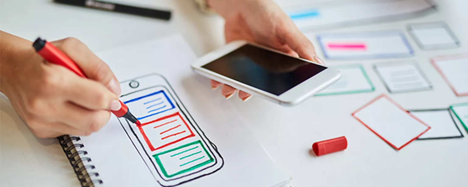 Image of a UX designer sketching while holding a smartphone.